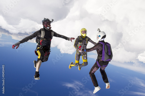 Three parachutists perform freestyle figures in free fall.
