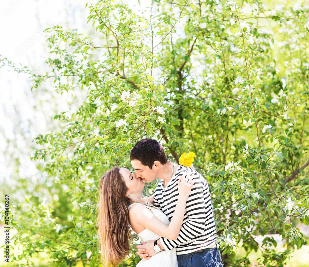 Loving couple under blossoming branches spring day. Young adult brunette man and woman kissing in fresh blossom apple or cherry trees garden. sweet kiss Loving couple under blossoming branches spring day. Young adult brunette man and woman kissing in fresh blossom apple or cherry trees garden. sweet kiss