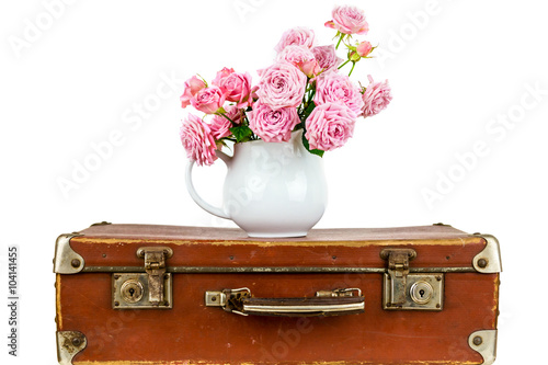 Pink flowers in jug on old brown vintage suitcase. Roses in jug. Pink roses. Shabby chic. Rustic concept.