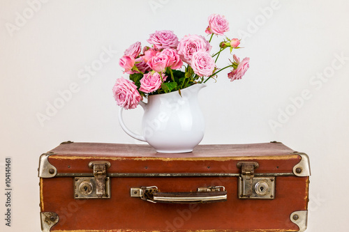 Pink flowers in jug on old brown vintage suitcase. Roses in jug. Pink roses. Shabby chic. Rustic concept.