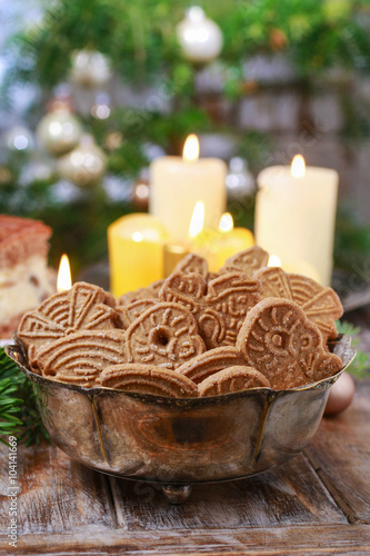 Bowl of speculaas biscuits, golden candles in the background.