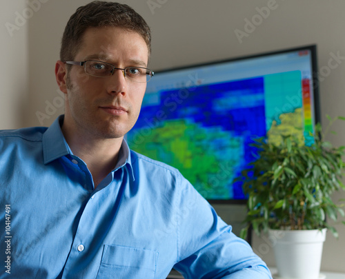 Obraz na plátně Handsome male meteorologist in glasses on his workplace.