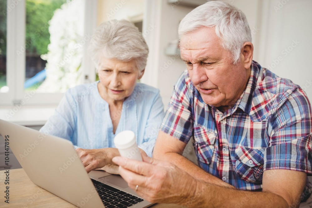 Senior couple holding a pill bottle while operating laptop Senior couple holding a pill bottle while operating laptop