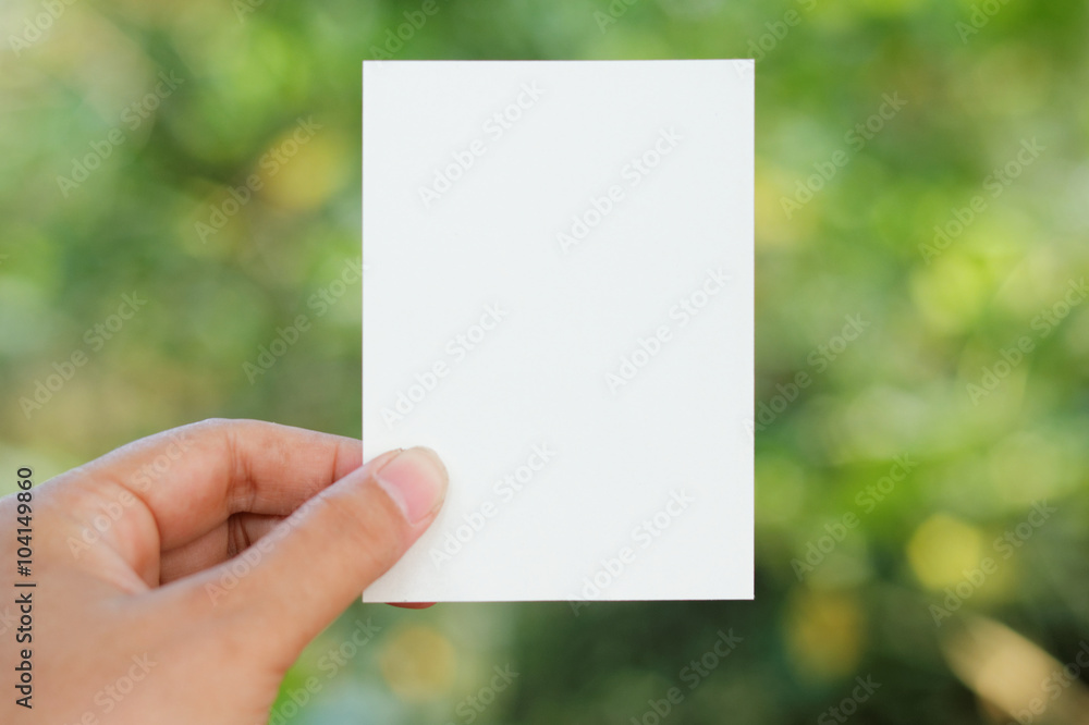 Hand holding a sheet of white paper with yellow and green Bokeh background Hand holding a sheet of white paper with yellow and green Bokeh background
