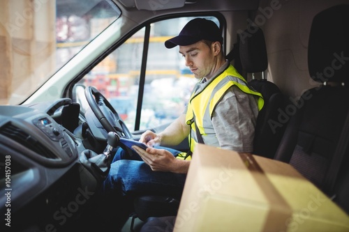 Slika na platnu Delivery driver using tablet in van with parcels on seat