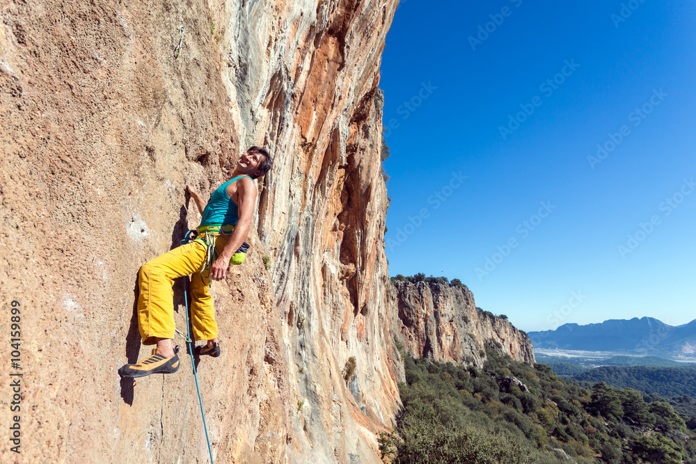 Smiling mature male extreme Climber hanging on rocky wall easy