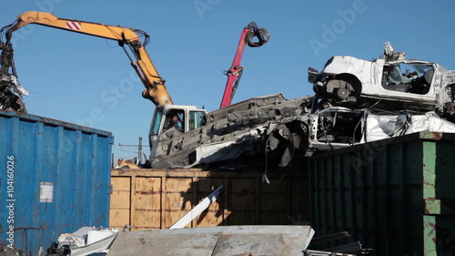 Cranes with hydraulic gripper moving scrap metal and smashed cars going to be shredded