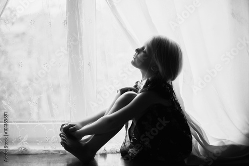 The child sits on a window sill, black and white
