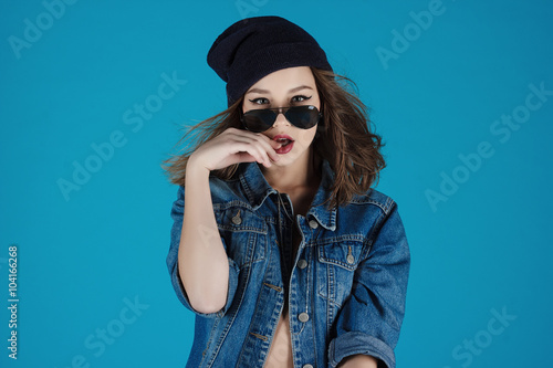 Closeup studio shot of pretty hipster teenage girl with beanie hat wearing jeans jacket looking at camera posing. © hermanshoroh