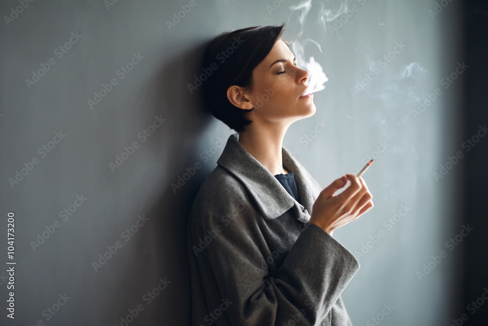 Portrait of fashionable woman smoking a cigarette on dark backgr - obrazy, fototapety, plakaty 