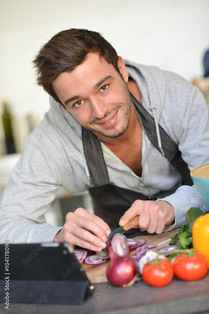 Fototapeta premium Portrait of a handsome young man cooking with digital tablet in
