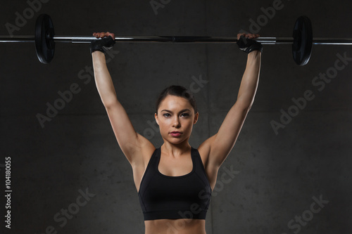 young woman flexing muscles with barbell in gym