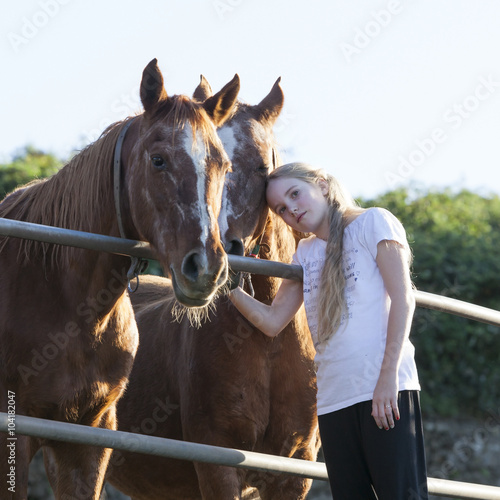 young blond girl poses with two brown horses