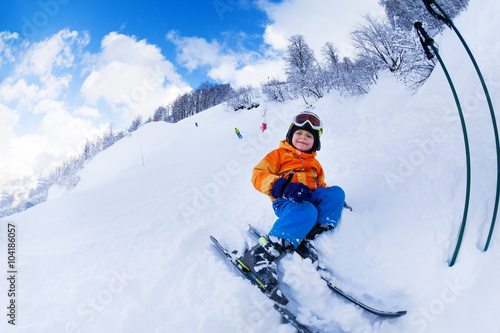 Little skier boy sit with ski in snow resting