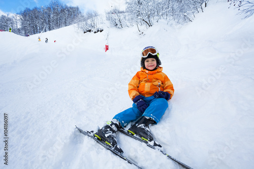 Little boy rest after ski lesson sitting in snow