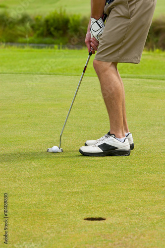 golfer putting on green, view from legs down