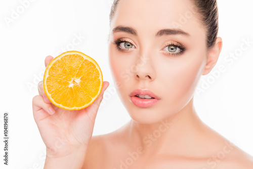 Attractive healthy young woman holding half of orange near her f