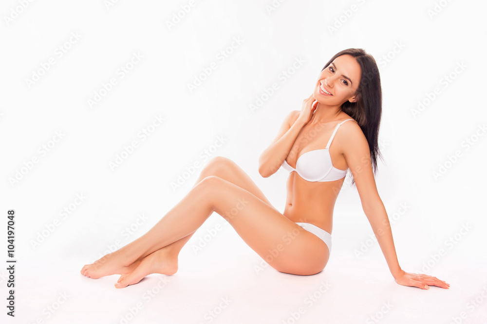 Smiling slim brunette sitting in lingerie on white background