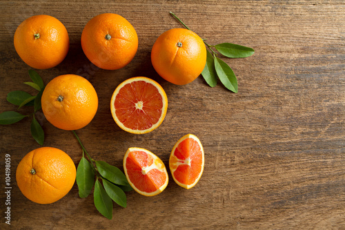 Fresh oranges with slices and leaves on wooden background.