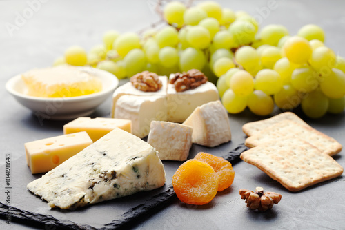 Glass of white wine and assorted cheese with grape on a slate background Copy space