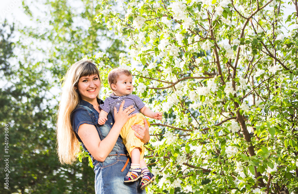 Fototapeta premium happy loving family with baby son in blooming spring garden. Mother holding baby. Spending time together outdoor. Mothers day holiday concept