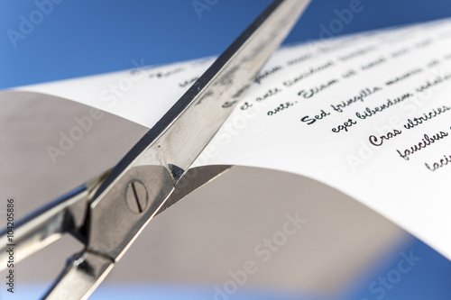 Close-up of scissors cutting a paper with dummy text, on blue background