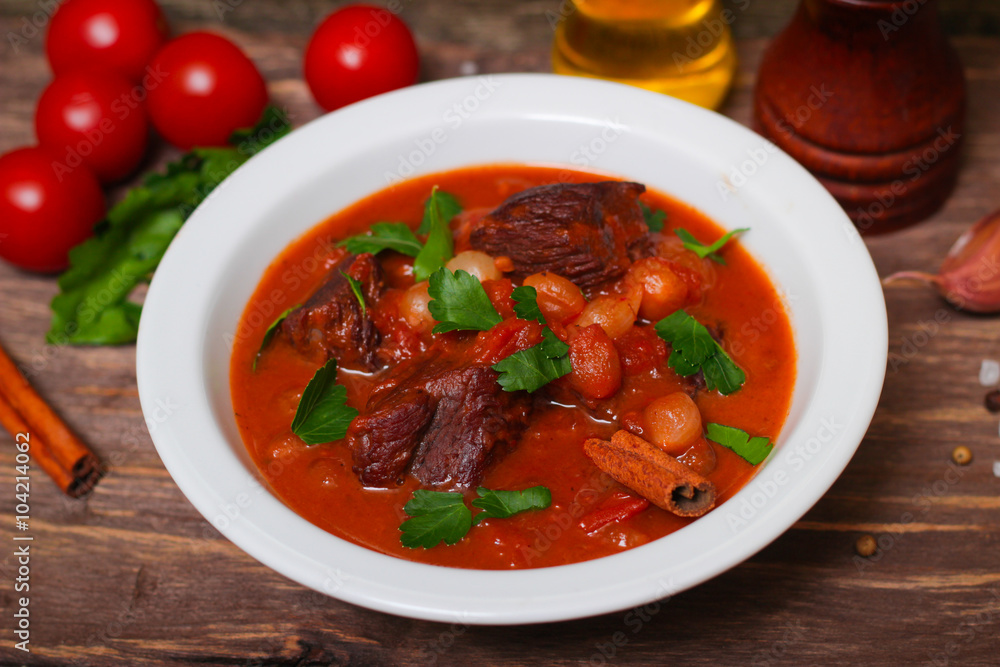 National Greek dish stifado with beef, tomatoes and onions, stewed in red wine with Herbs on a wooden background, horizontal National Greek dish stifado with beef, tomatoes and onions, stewed in red wine with Herbs on a wooden background, horizontal