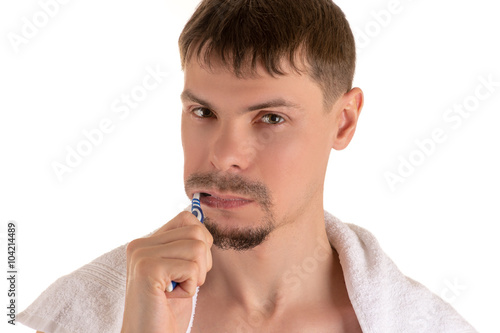 Portrait of an adult man cleaning his teeth with toothbrush and white towel on his shoulders looking at camera