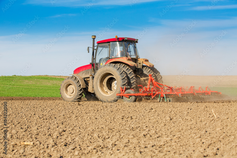 Obraz premium Tractor cultivating field at spring