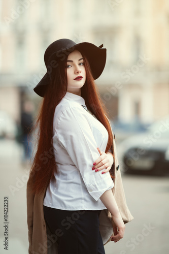 Portrait of young beautiful lady wearing stylish classic clothes posing at street of the old city. Girl looking at camera. Plus size model. Female fashion concept. Close up. Toned
