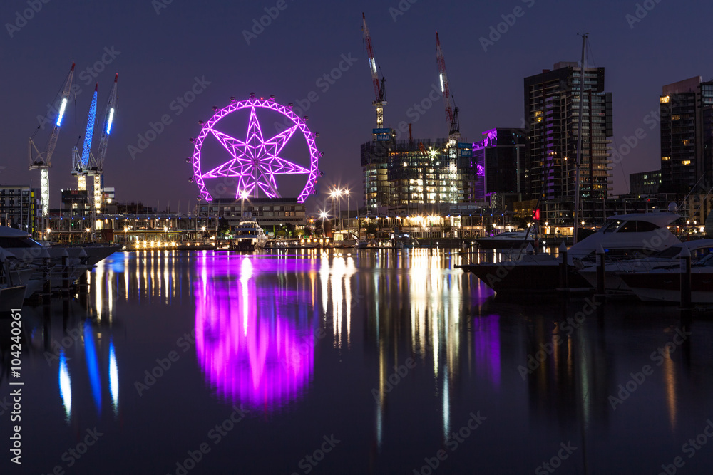 Fototapeta premium Melbourne, Australia - Feb 21 2016: Observation wheel lit in purple in Docklands, Melbourne with reflections in Yarra river. Night scene.