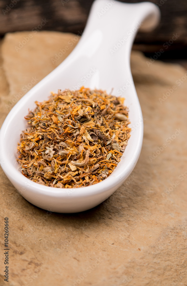 Calendula Marigold flowers in white spoon on stone Calendula Marigold flowers in white spoon on stone
