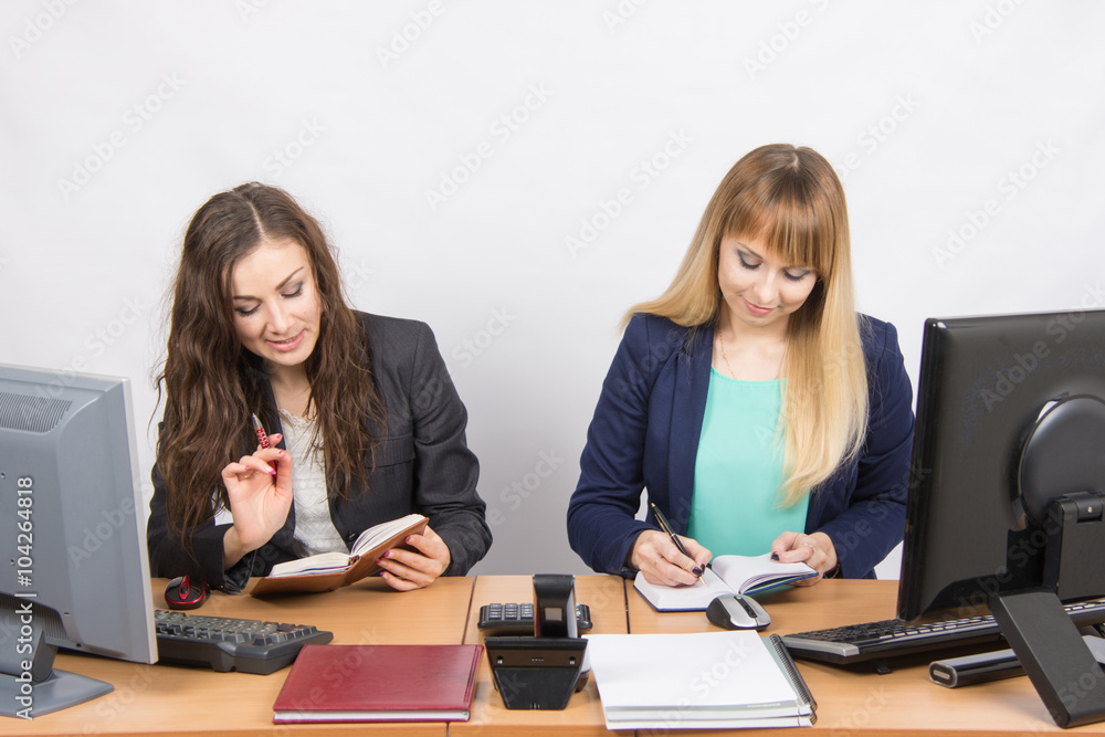 Two business women looking at diaries and make a plan of the day Two business women looking at diaries and make a plan of the day