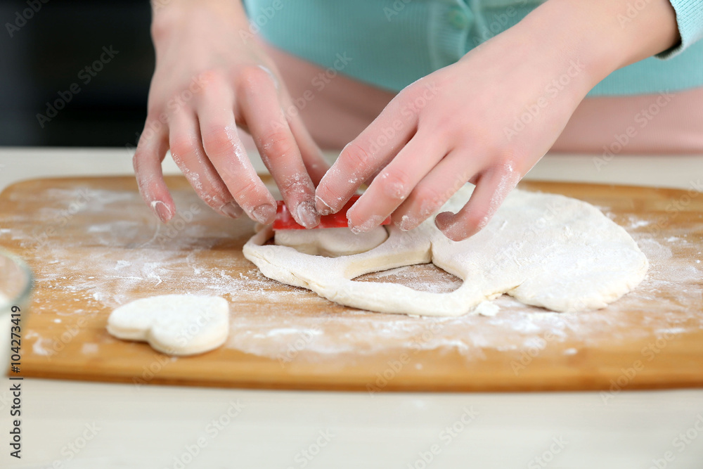 Young woman cutting out the hearts in a dough on the kitchen counter