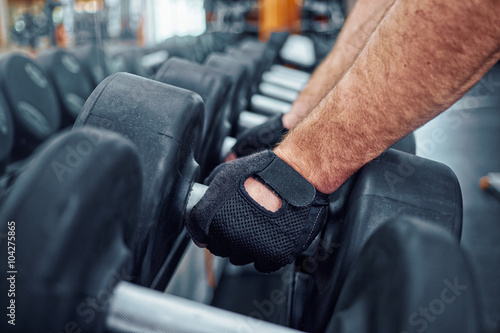 Hand of a man taking a dumbbell out of set of black weights
