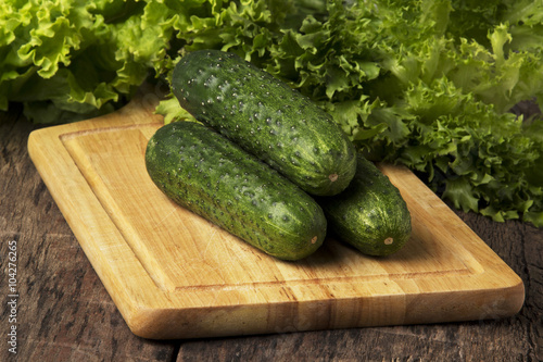 green cucumbers with lettuce on wooden board