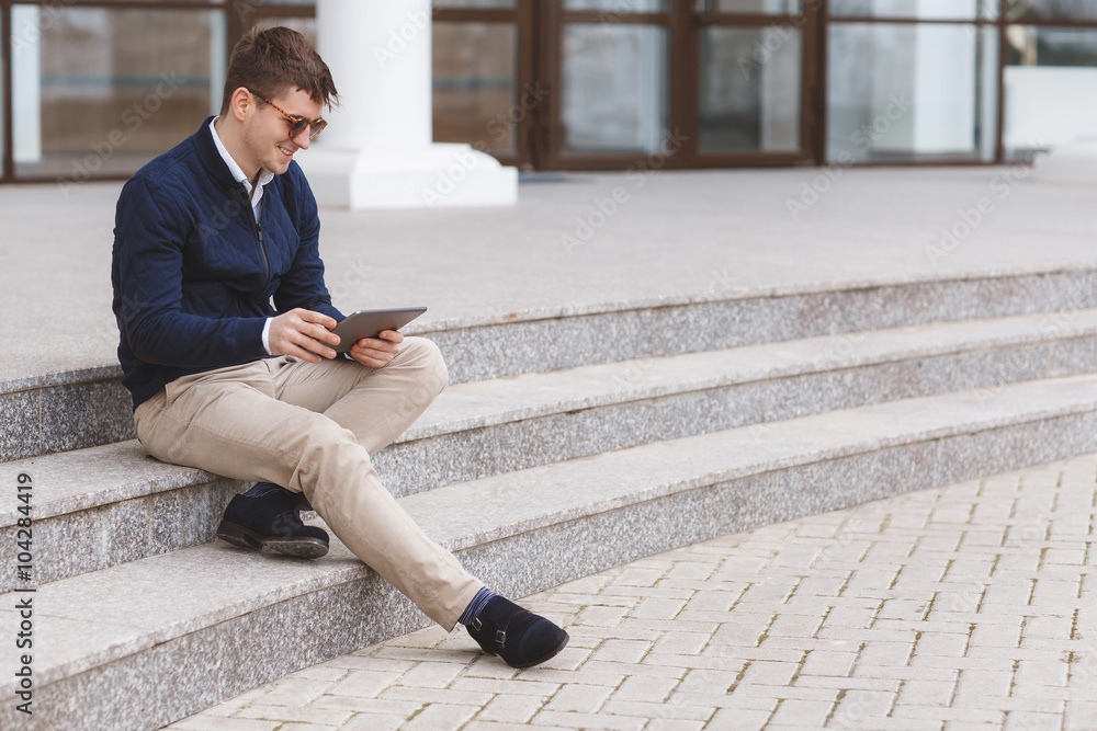 Young man with tablet computer sitting on stairs