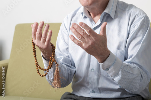 Praying hands of an old man holding rosary beads. S