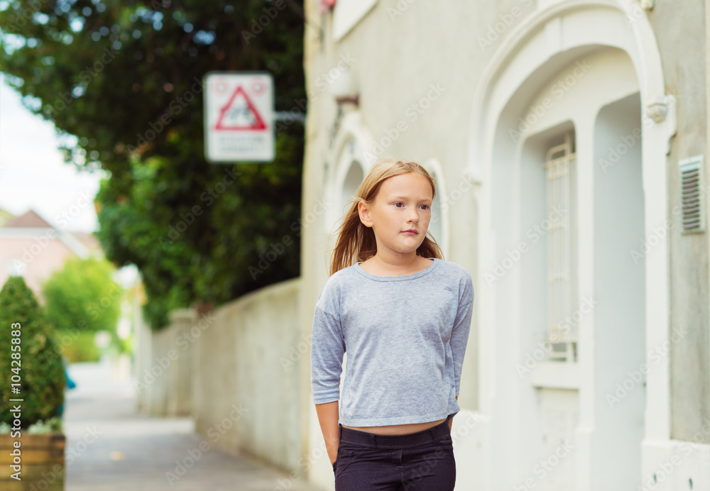 Fashion portrait of cute little girl of 7-8 years old, walking down the street, wearing grey top, toned image