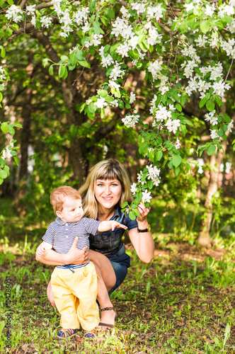 Happy young woman and little son in the blooming spring garden. Mothers day holiday concept