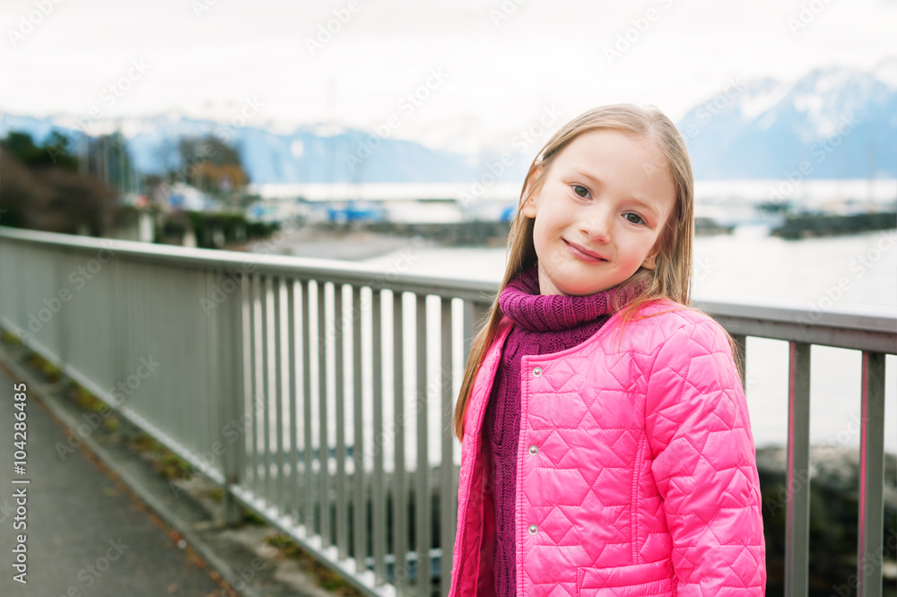 Outdoor portrait of a cute little girl, having promenade by the lake, wearing bright pink pullover and jacket Outdoor portrait of a cute little girl, having promenade by the lake, wearing bright pink pullover and jacket