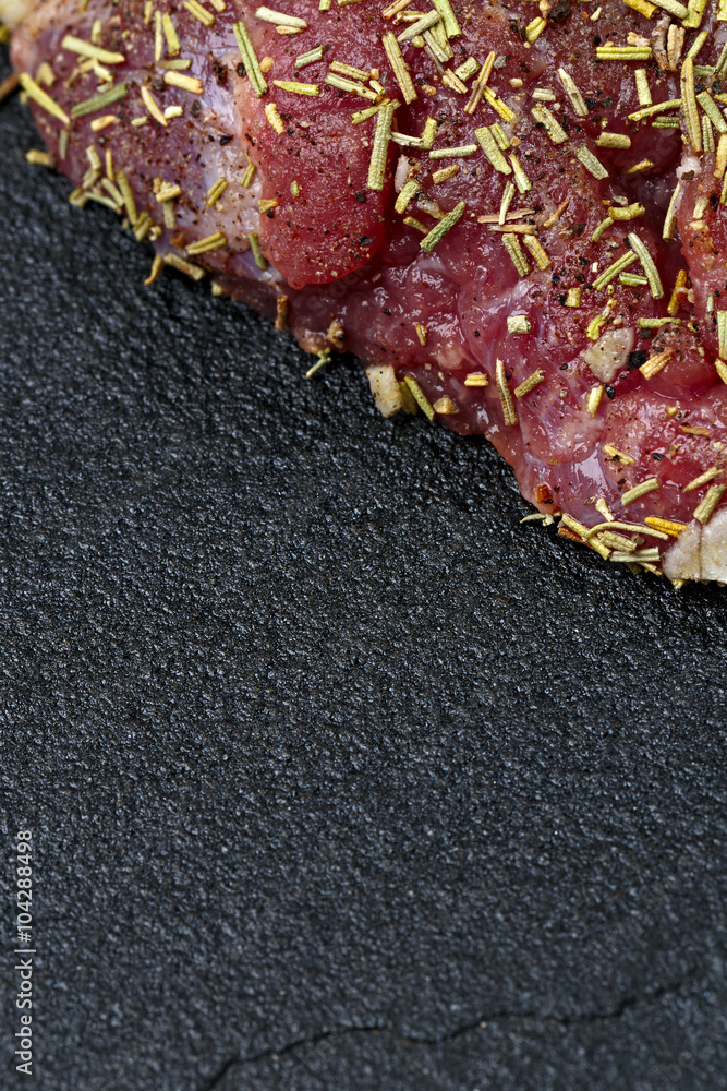 Raw meat on a dark background with spices prepared for grilling.