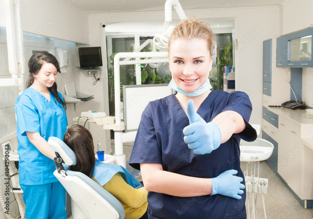 Obraz premium Confident smiling female dentist thumb up in her dental office