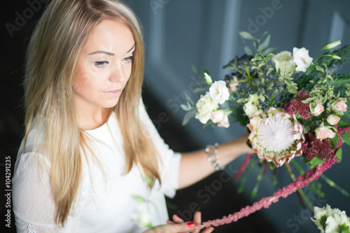 Florist at work  pretty young blond woman making fashion modern bouquet of different flowers