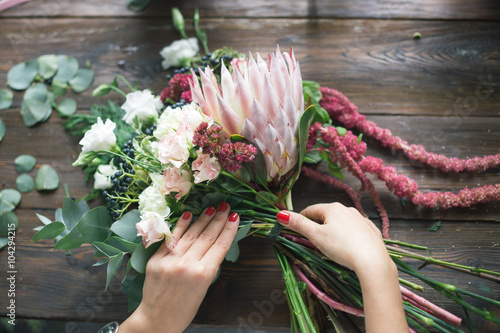 Florist at work: pretty young blond woman making fashion modern bouquet of different flowers