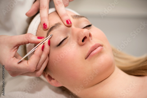 Plucking eyebrows with tweezer by beautician in beauty salon.