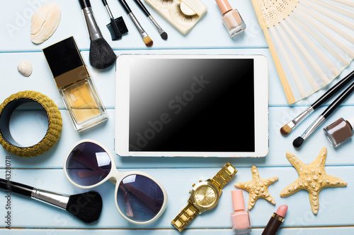Summer women's accessories: tablet and cosmetics on blue wood background.