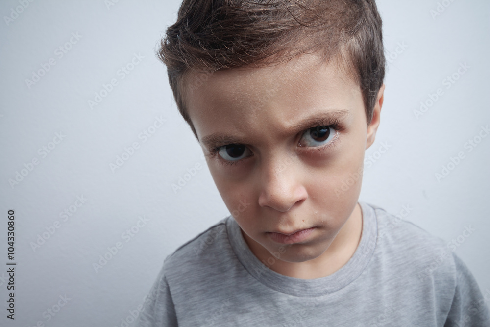Boy close-up portrait with a serious expression on gray backgrou Boy close-up portrait with a serious expression on gray backgrou