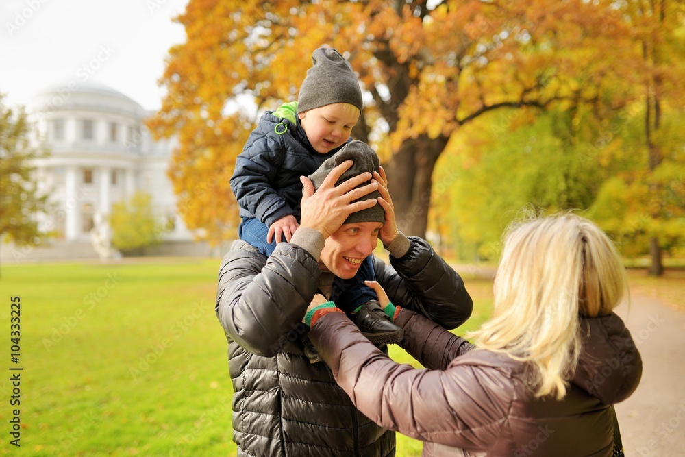Fototapeta premium Wife corrects clothes for husband with child on a shoulders in park