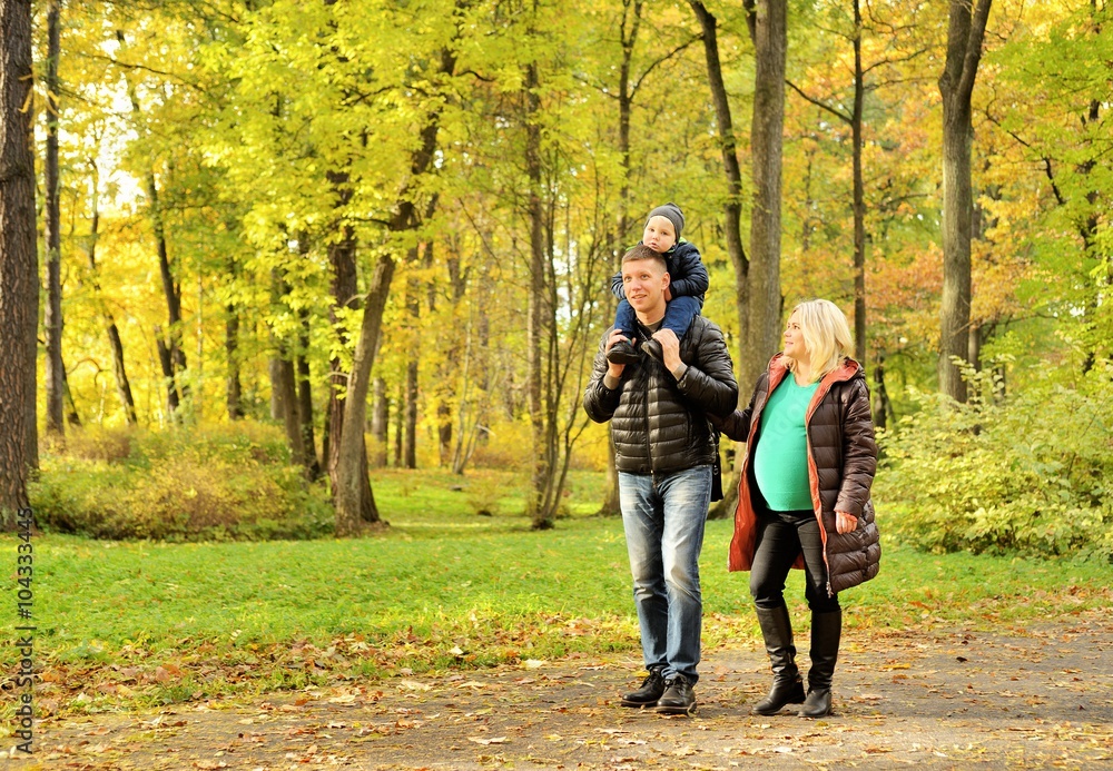 Pregnant young woman walking in autumn park with her husband and child Pregnant young woman walking in autumn park with her husband and child